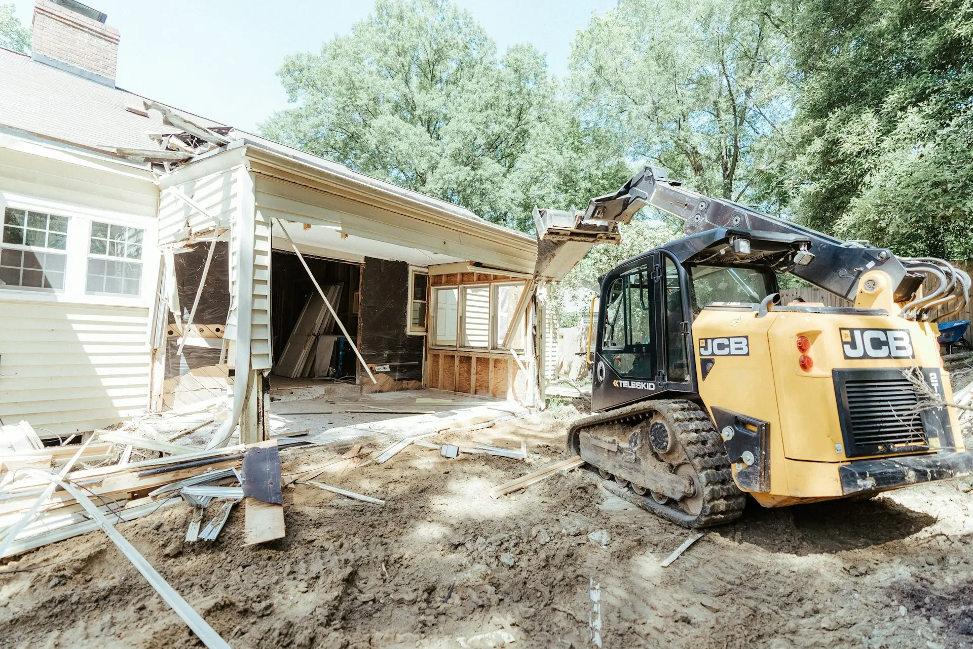Demolition of a house extension with a JCB track loader, showing the beginning of a home renovation project.